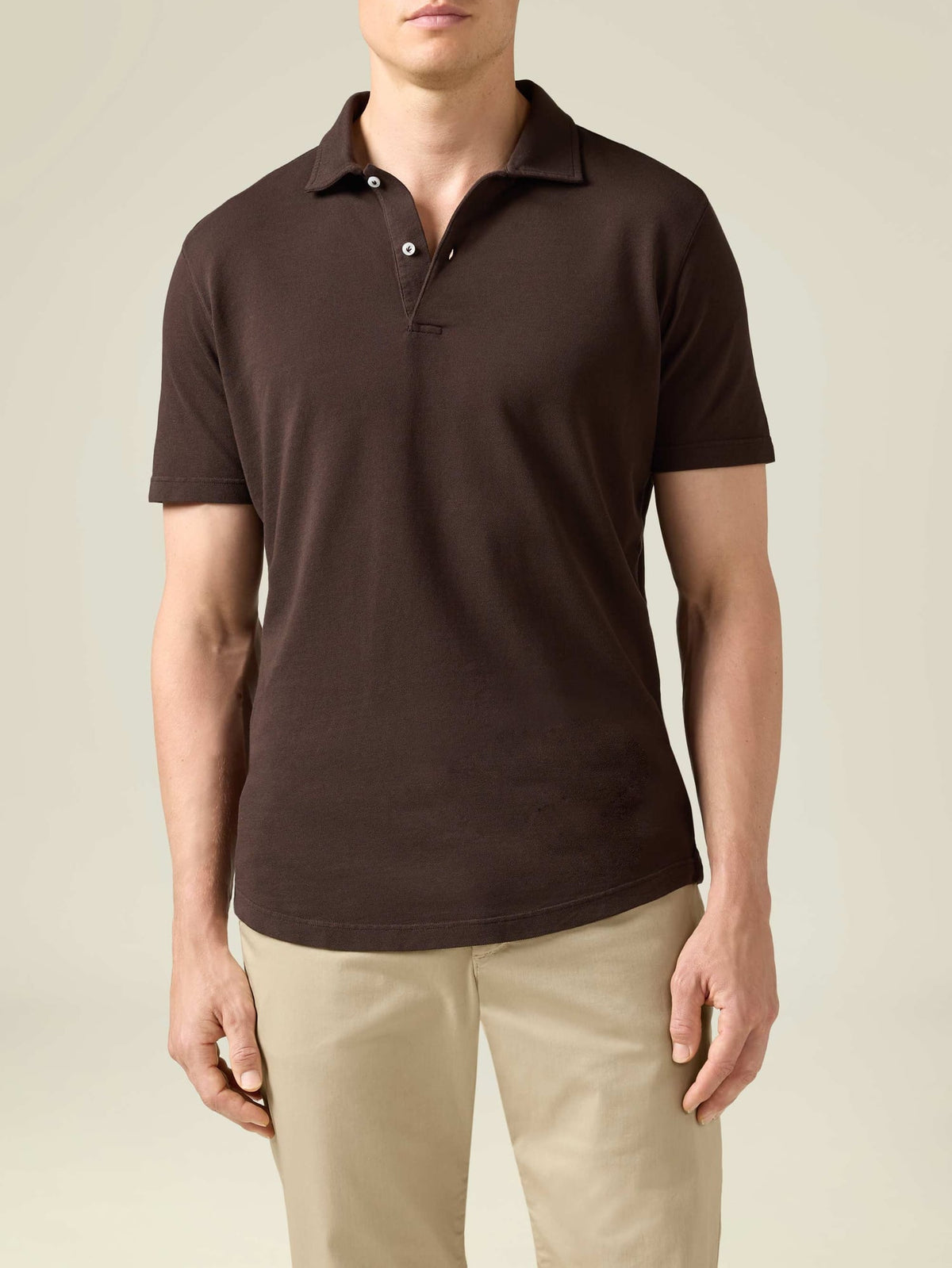 A model wears the Classic Piqué Polo in Chocolate Brown, shown with light beige trousers.