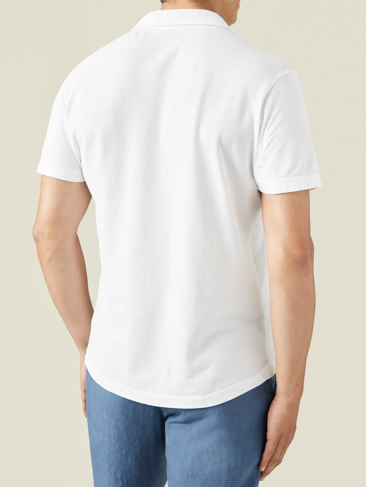 Back view of a man wearing the Classic Piqué Polo in white, highlighting the shirt's relaxed fit and rounded hem.