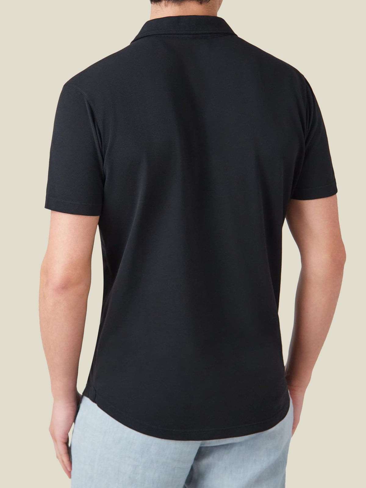 Rear view of a model wearing the Black Classic Piqué Polo, showcasing its relaxed silhouette and curved hemline.