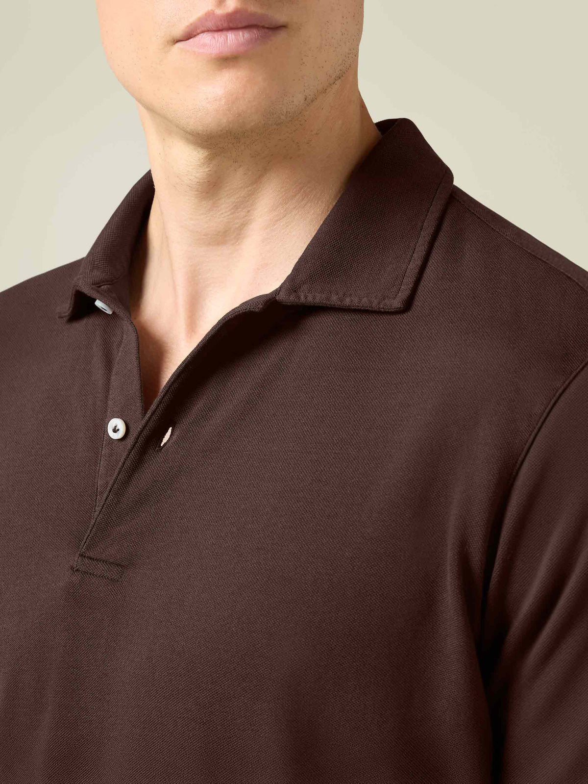 A close-up of the Classic Piqué Polo in Chocolate Brown, detailing the textured fabric, collar, and mother-of-pearl button.
