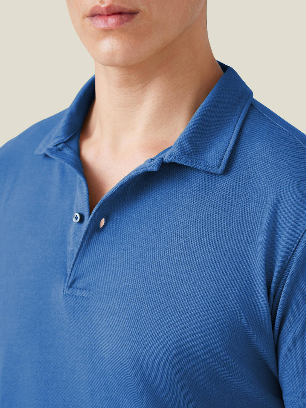 A close-up of a model wearing the royal blue Classic Piqué Polo, focusing on the collar, placket, and piqué fabric texture.