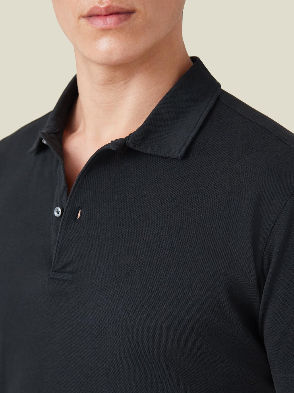 Close-up of the black piqué cotton polo shirt, highlighting the classic collar and mother-of-pearl button placket.