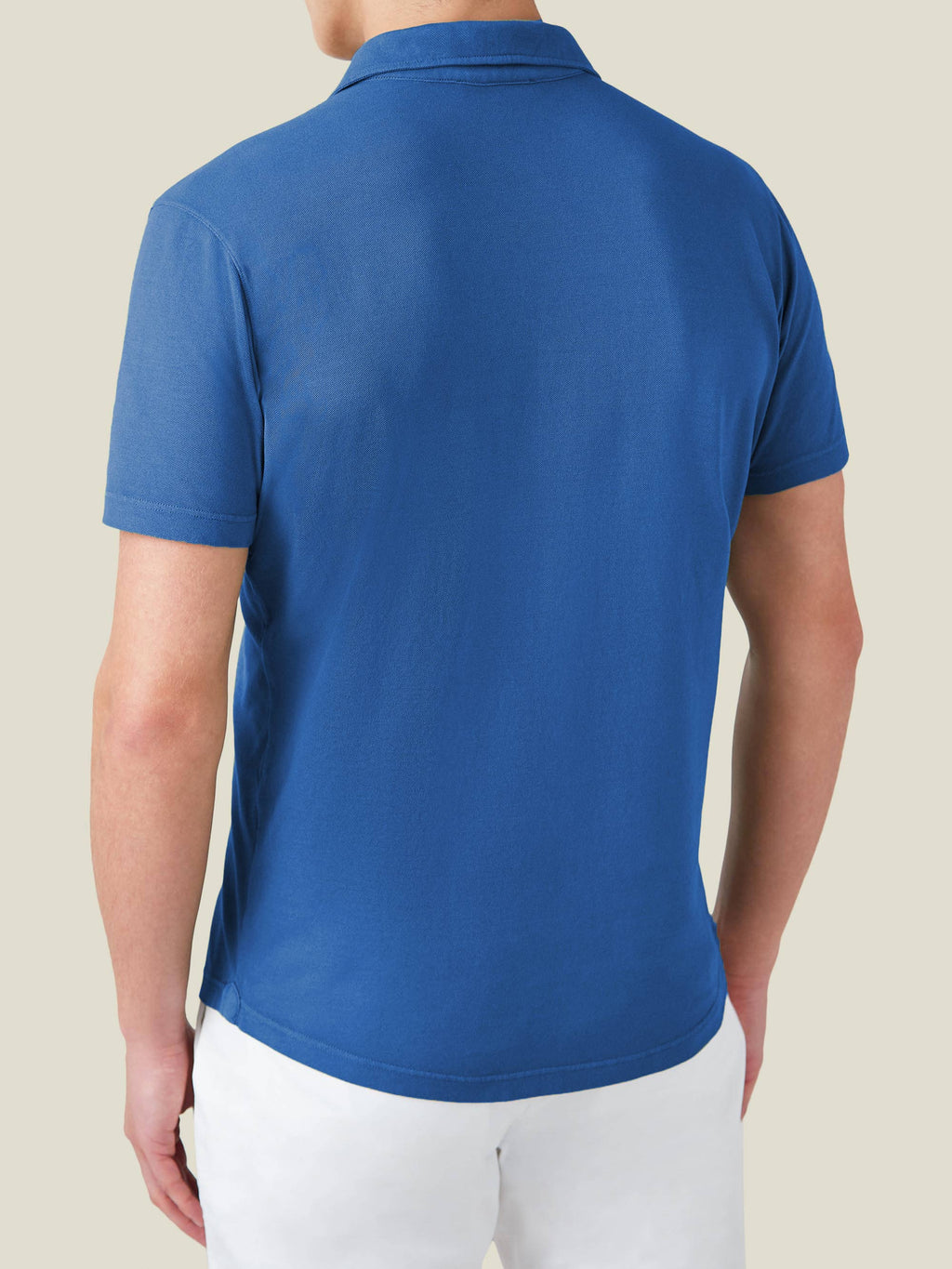 Back view of a model wearing the Classic Piqué Polo in royal blue, styled with white trousers.