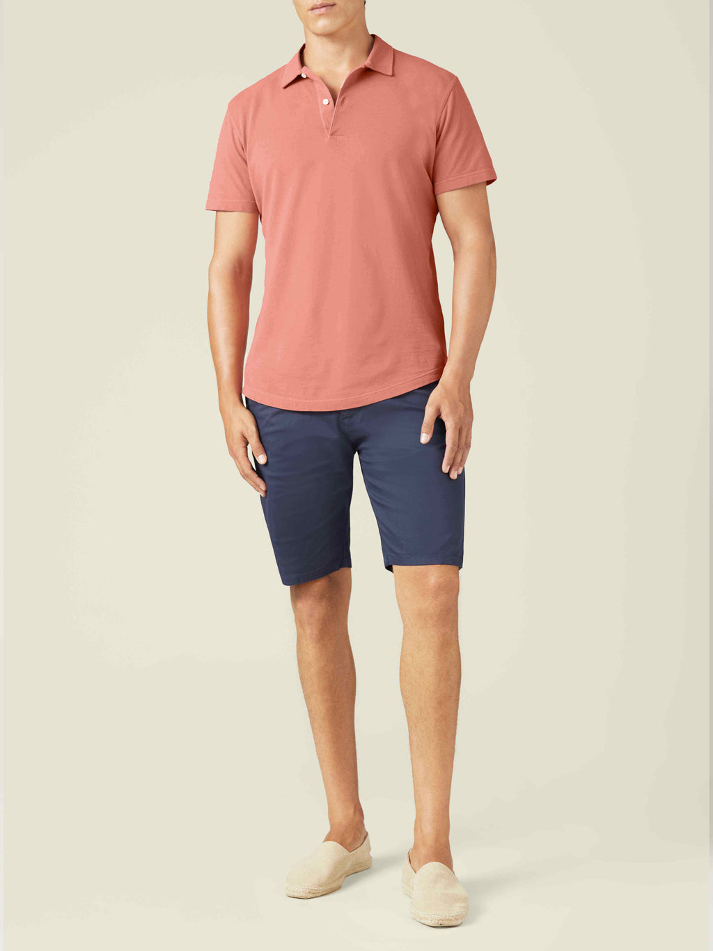 A front view of a model wearing the Luca Faloni Classic Piqué Polo in peach, styled with navy shorts and beige loafers.