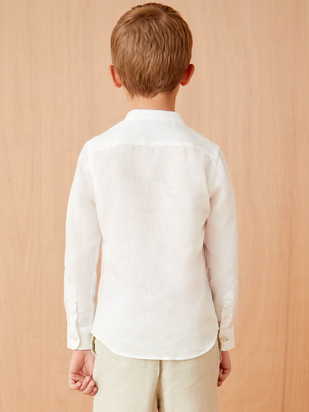 Back view of a boy wearing the white Versilia Junior Linen Shirt, showcasing the band collar and clean silhouette.