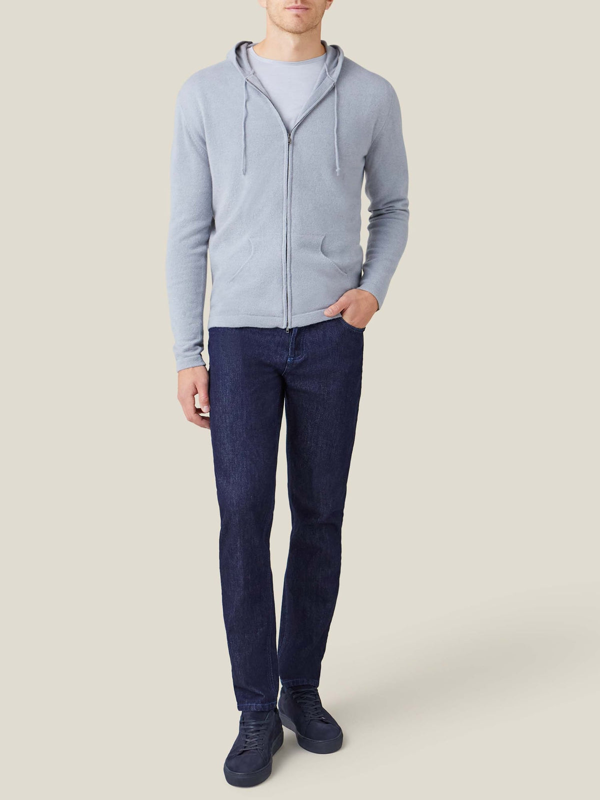 A man wearing the light grey silk-cotton long-sleeved T-shirt, styled under a zip-up hoodie and paired with dark jeans.
