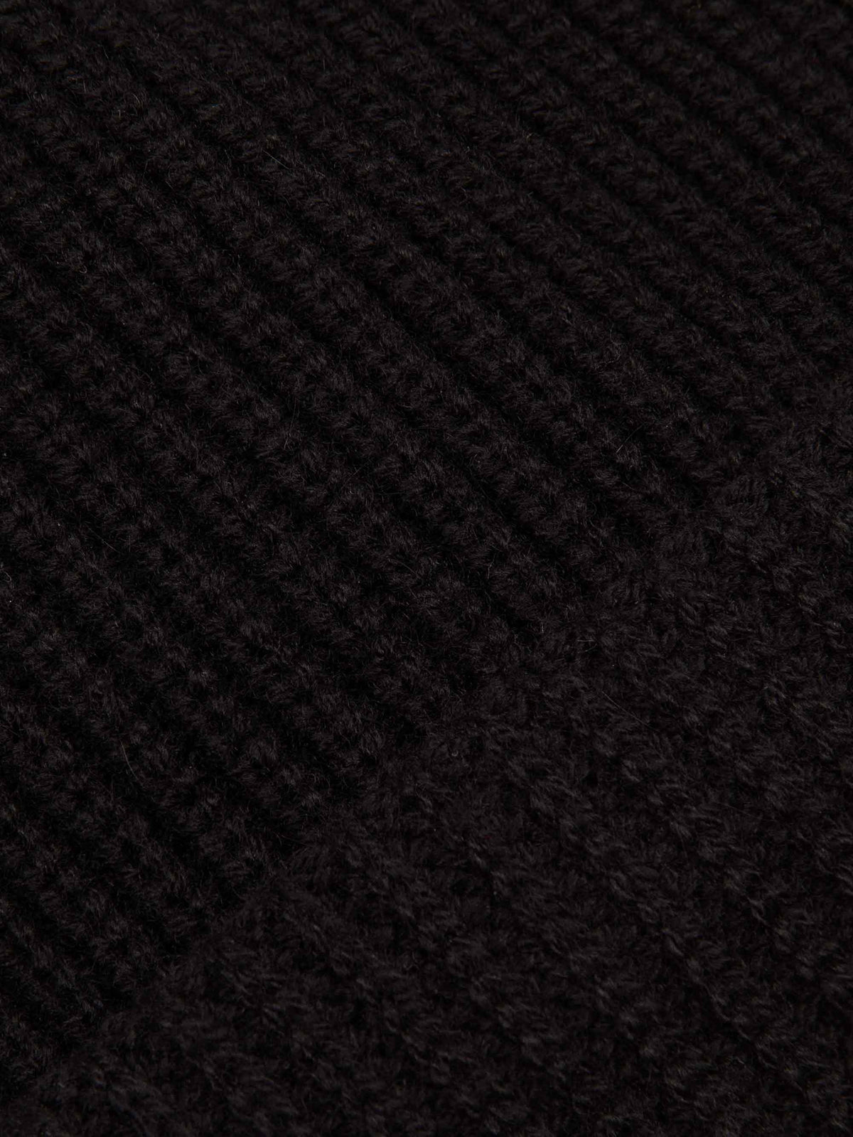 A close-up of the chunky ribbed knit texture of the black four-ply cashmere Chunky Knit Beanie.