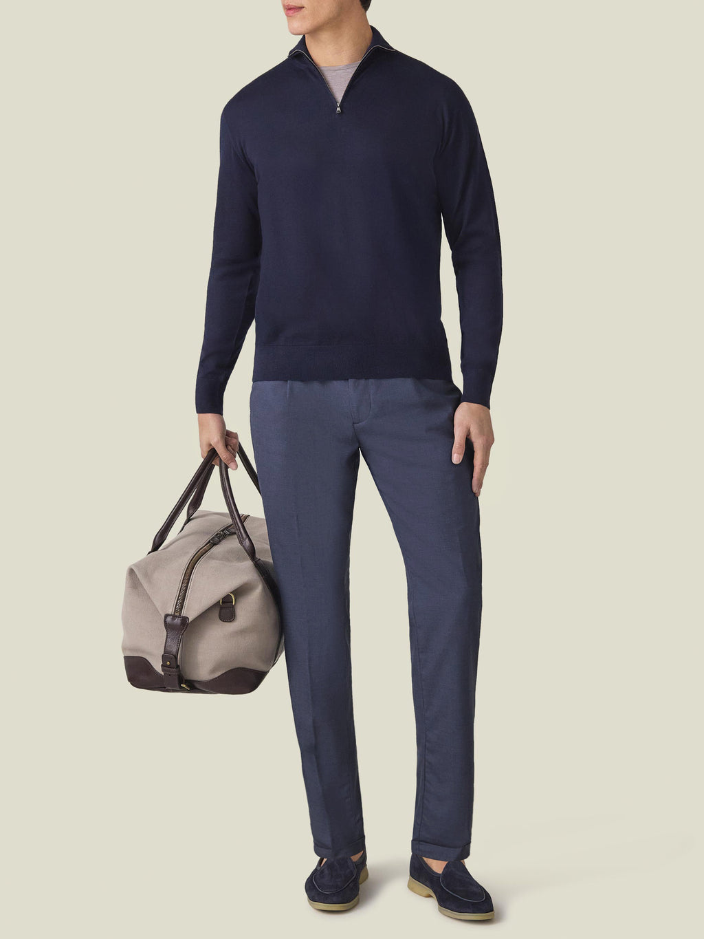 Model wearing the Lightweight Wool Trousers in Classic Blue with a navy zip sweater and loafers, holding a travel bag.