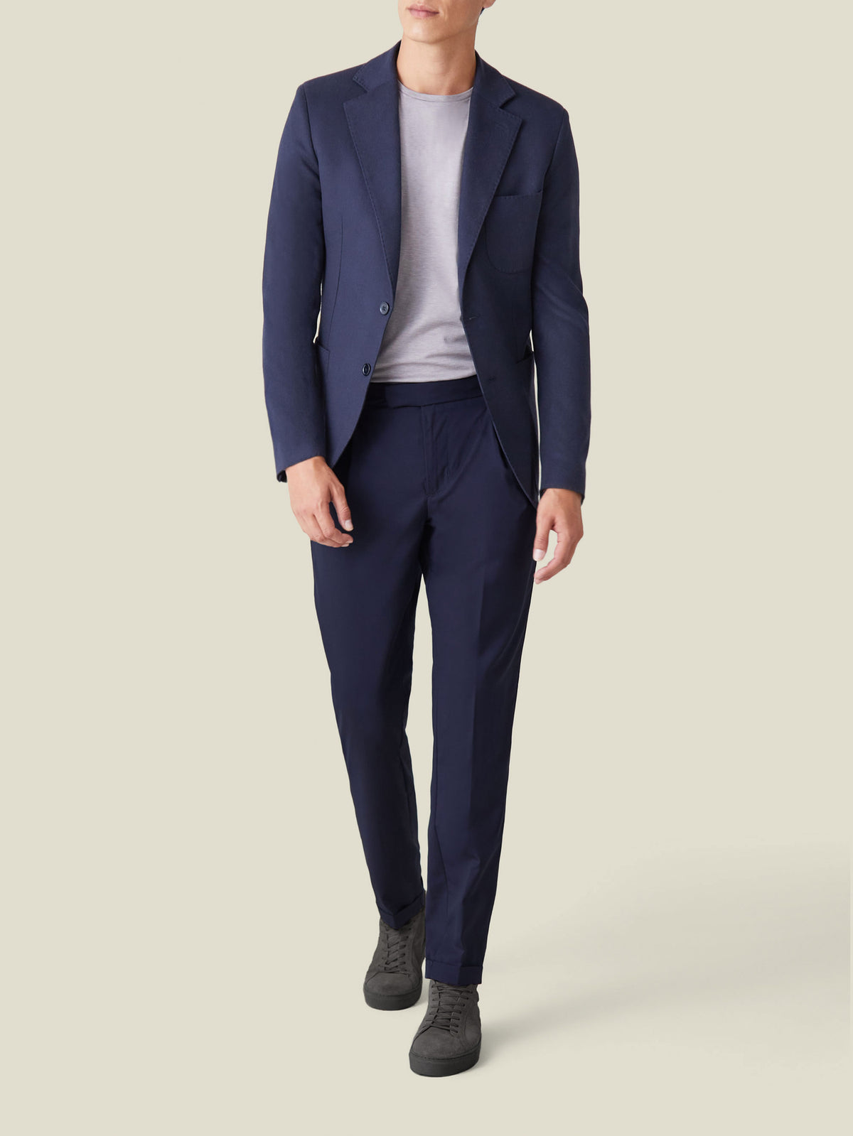 Model wearing Luca Faloni's navy Lightweight Wool Trousers with a matching blazer, grey t-shirt, and grey sneakers.