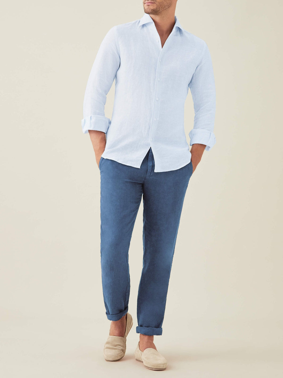 Model wears the Luca Faloni Portofino Linen Shirt in Striped Sky Blue, paired with dark blue trousers and beige loafers.