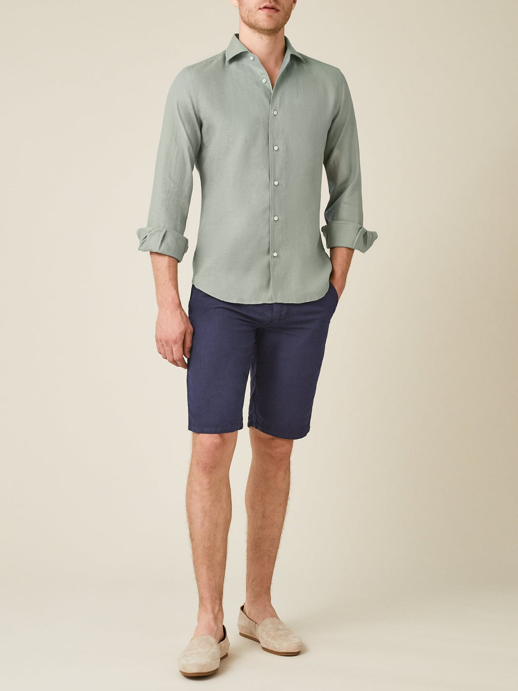 A man models the Portofino Linen Shirt in Sage Green, styled with navy shorts and loafers against a plain background.