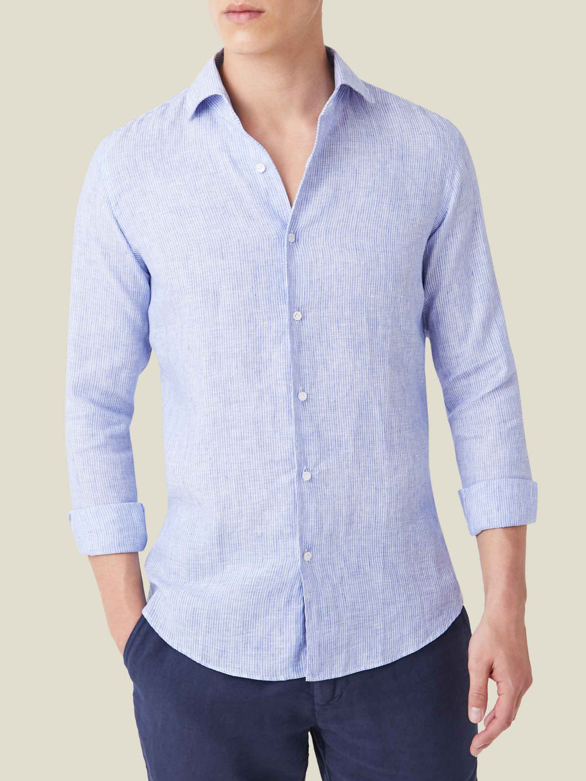 Front view of a model wearing the Portofino Linen Shirt in Striped Classic Blue with sleeves rolled up and navy trousers.