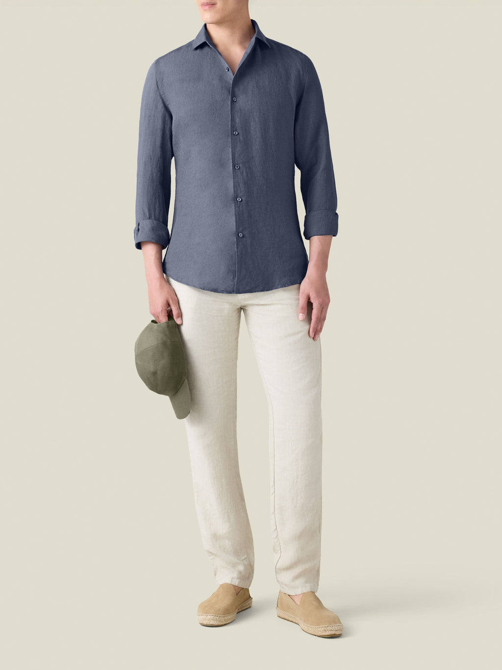 Model wearing the Payne's Grey Portofino Linen Shirt with off-white trousers and espadrilles, holding a cap.