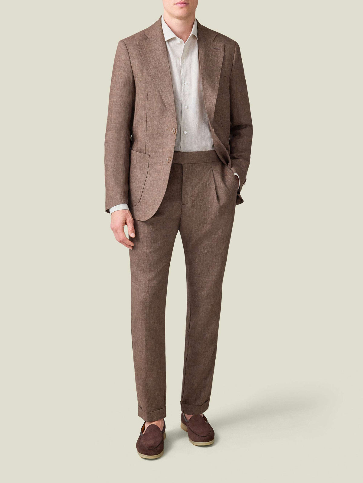A model wearing the Sand Portofino Linen Shirt tucked into pleated brown linen trousers and under a matching blazer.