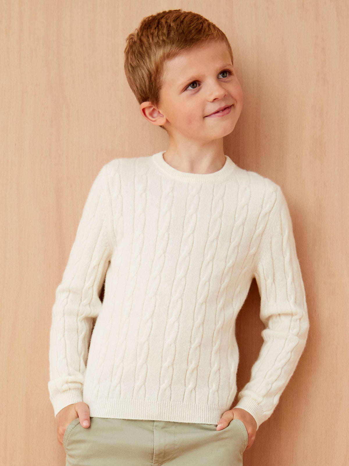 A child model wears the Ivory Junior Cable Knit, showcasing its classic crew neckline and intricate cable knit texture.