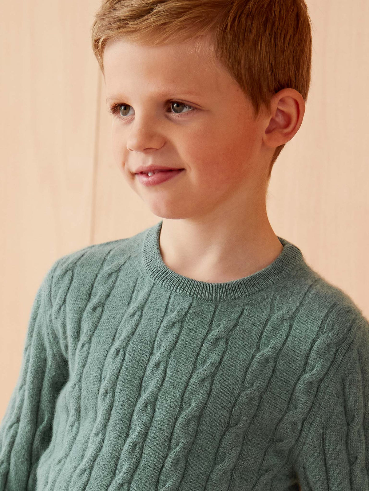 A close-up of a young boy wearing the Junior Cable Knit in Marine Green cashmere, highlighting its detailed knit texture.