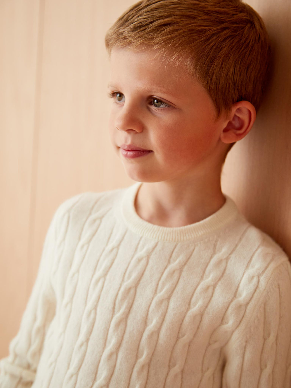 A close-up of a young boy wearing the Luca Faloni Junior Cable Knit in Ivory, highlighting the detailed cable knit pattern.