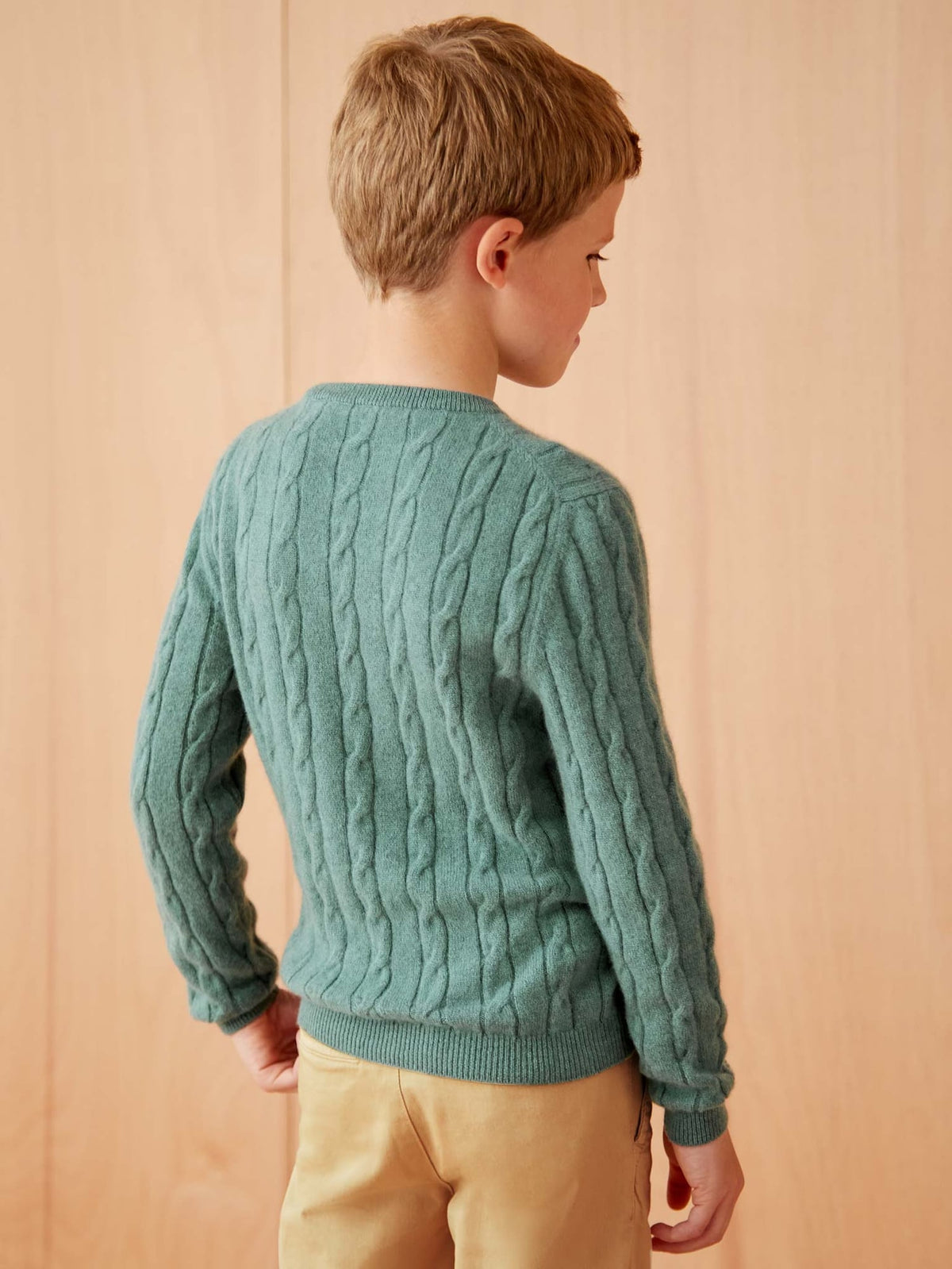 Rear view of a boy wearing the Marine Green Junior Cashmere Cable Knit, showcasing the sweater's signature cable pattern.