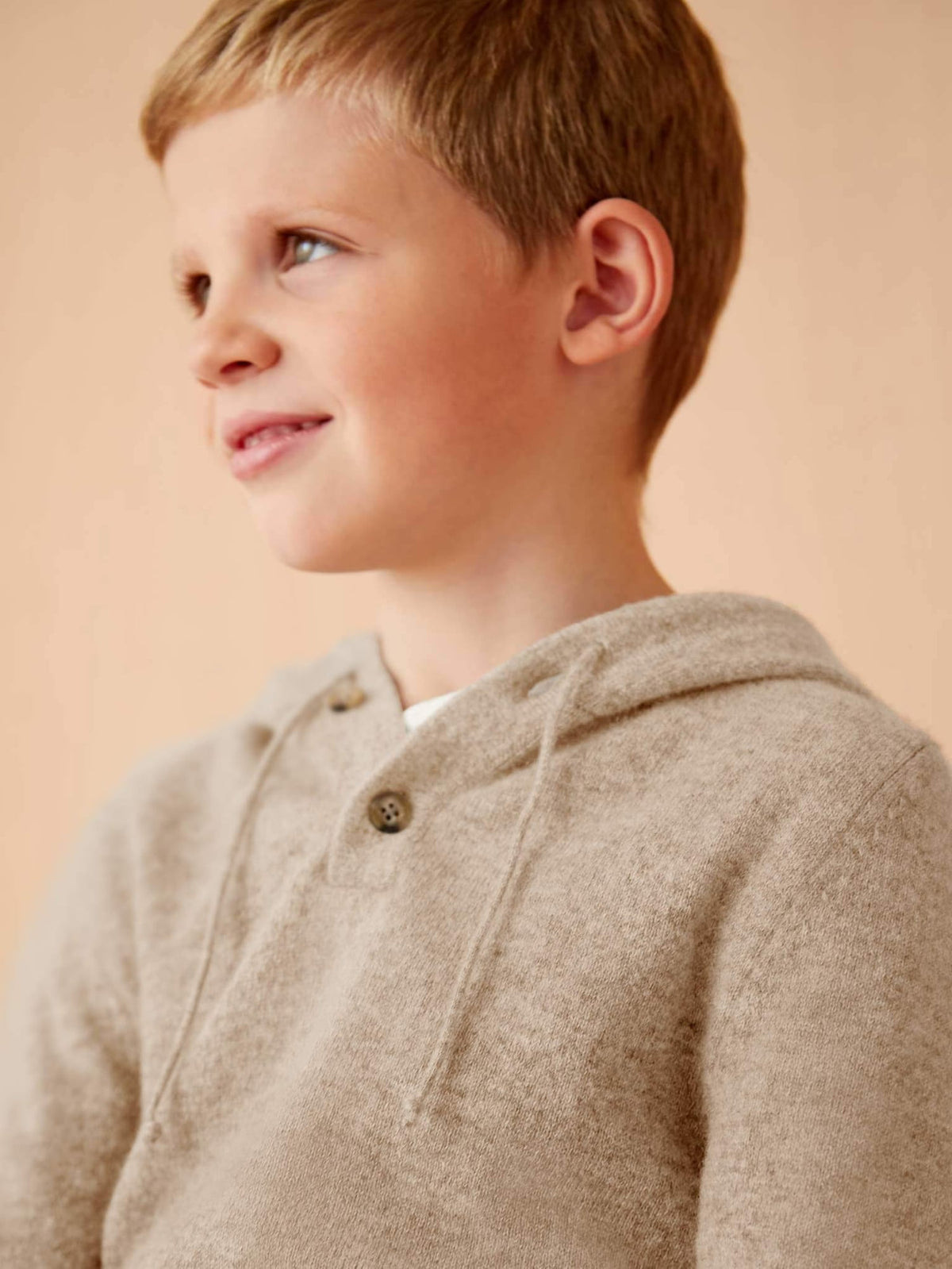 A close-up of a boy wearing the camel beige Junior Cashmere Hoodie, focusing on the soft texture and horn button detail.