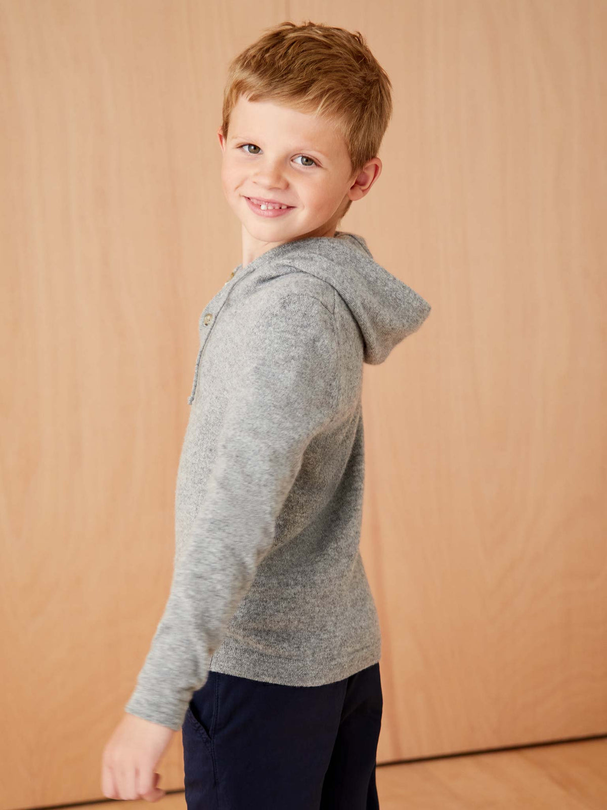Side profile of a young boy smiling while wearing the Dolomiti Grey Junior Cashmere Hoodie from Luca Faloni.