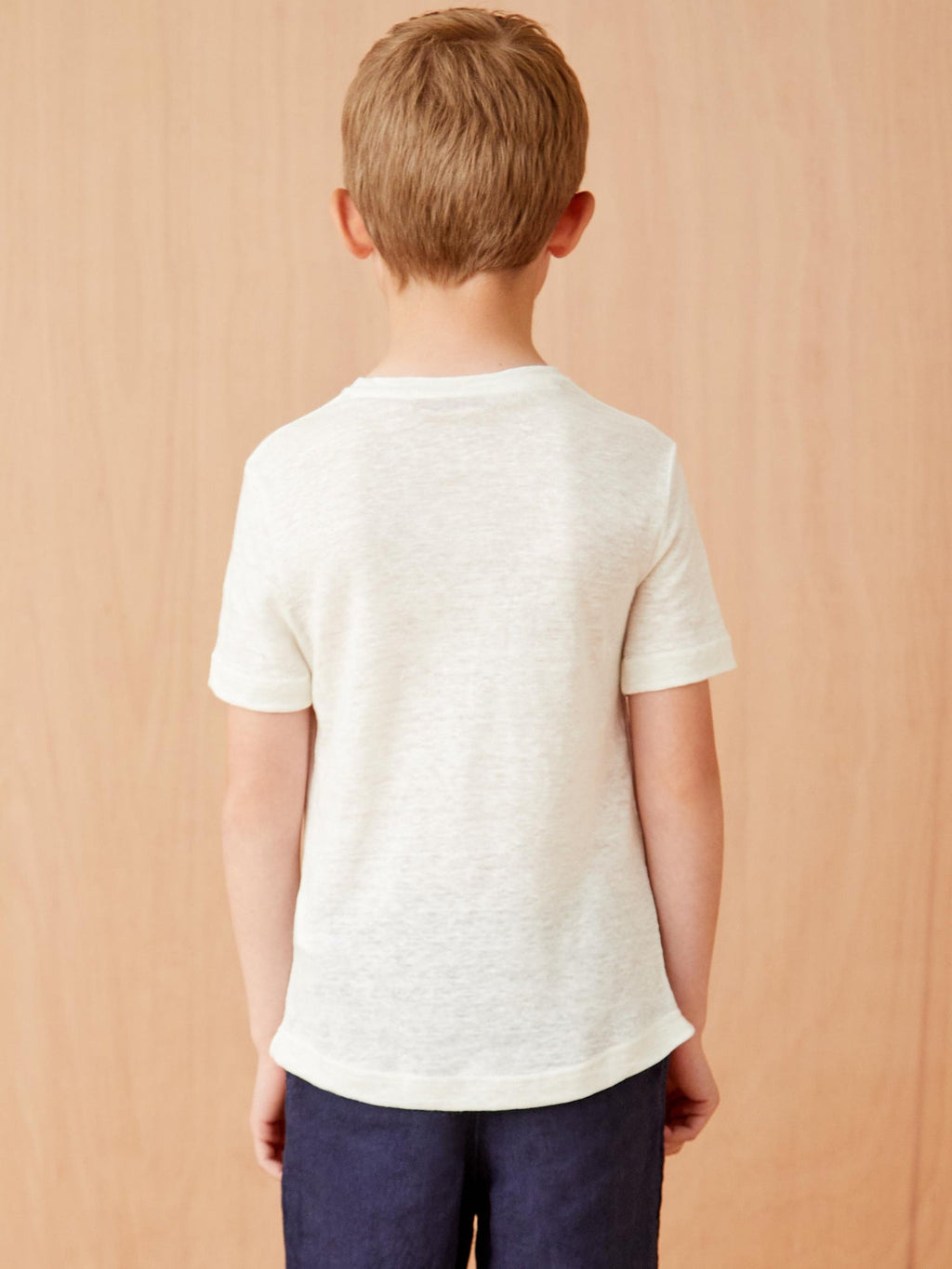 Back view of a young boy wearing the cream Junior Linen Jersey T-Shirt, showcasing its relaxed fit and rounded hemline.