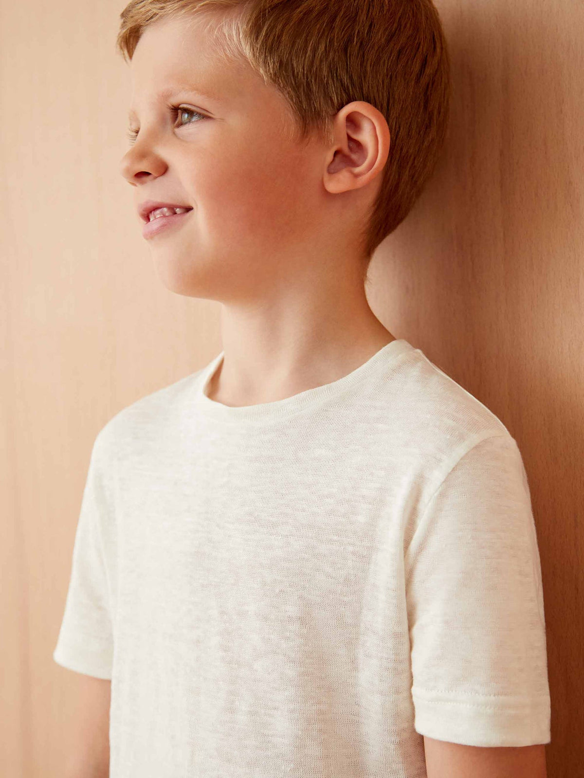 A close-up profile of a young boy wearing the cream Junior Linen Jersey T-Shirt, highlighting its soft texture.