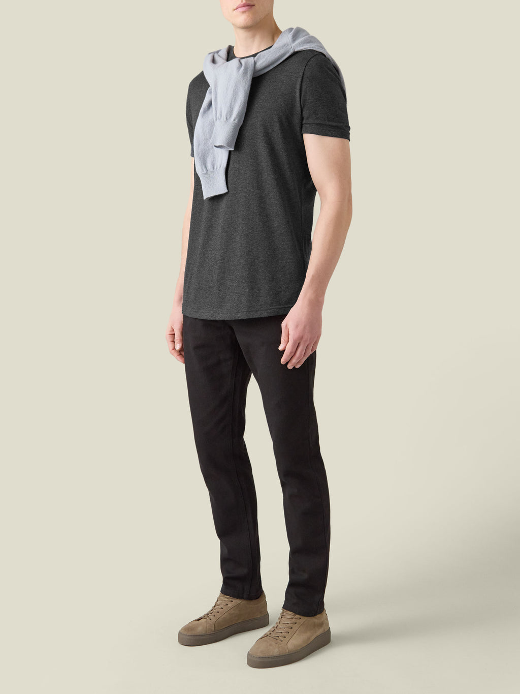 Model wearing the Charcoal Grey Cashmere Cotton T-Shirt with black trousers and a light grey sweater over his shoulders.