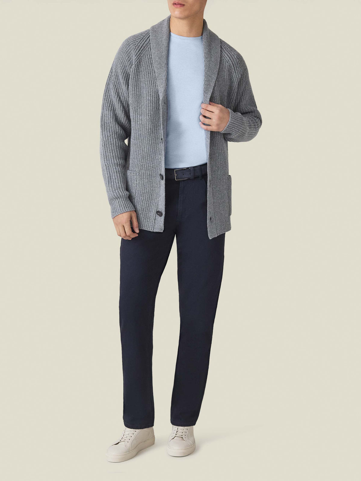 Model wears the Light Blue Cashmere Cotton T-Shirt layered under a grey cardigan with navy trousers and white sneakers.