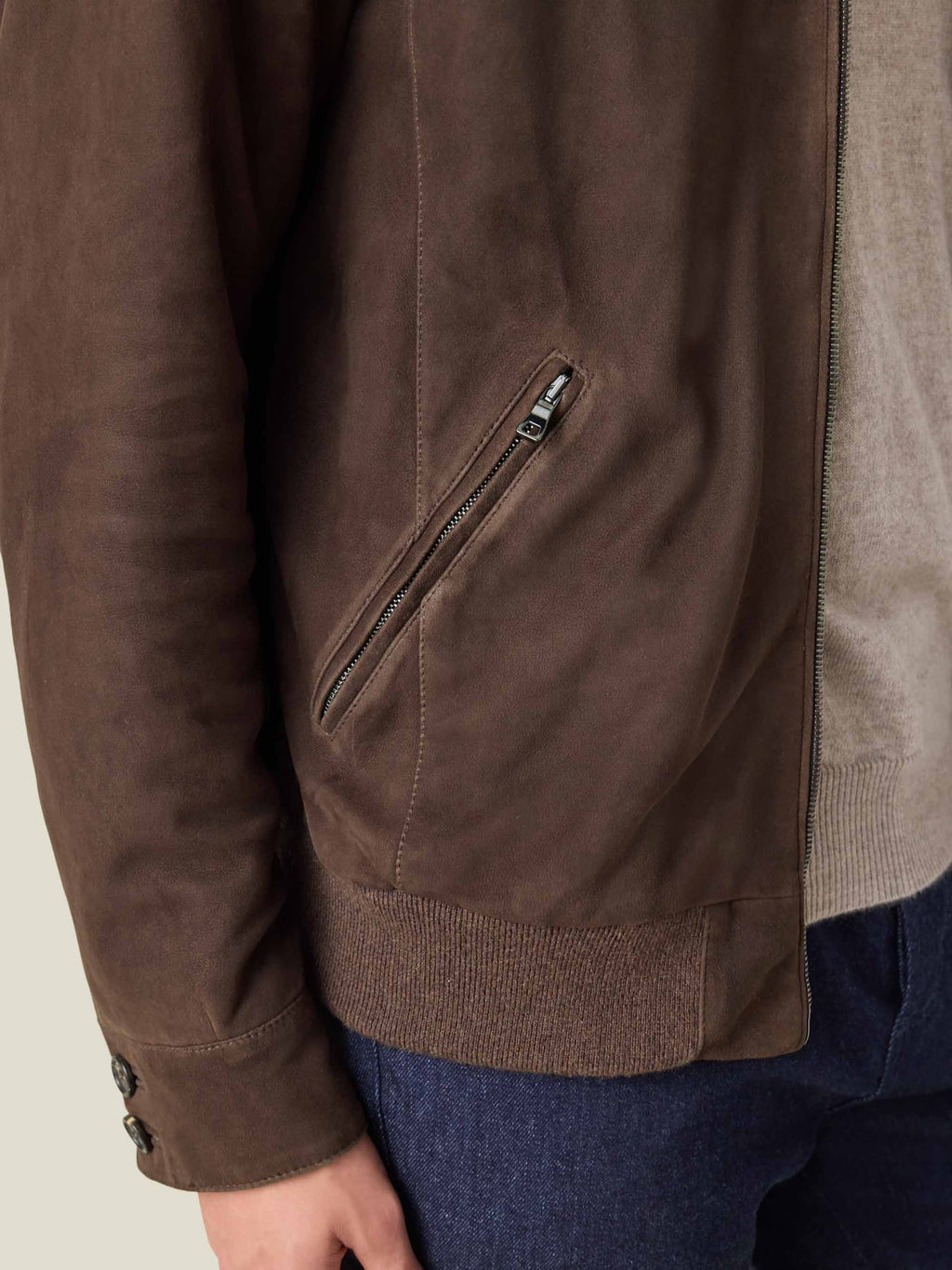 A close-up detail of the chocolate brown Classic Bomber Jacket, showing the goatskin suede, zipped pocket and cashmere hem.