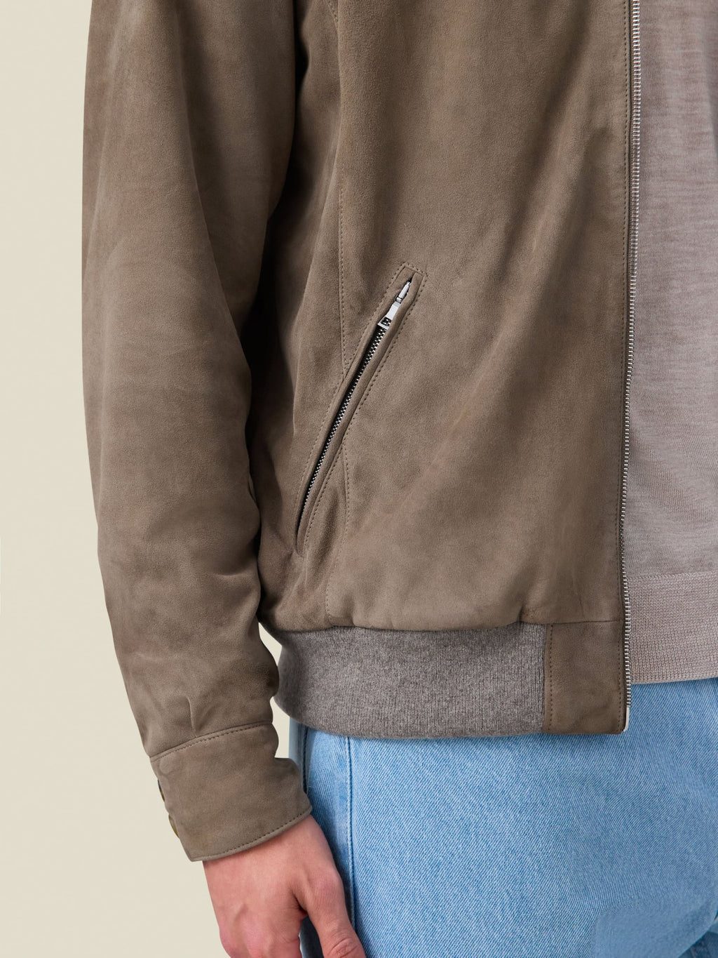 A close-up side view of the Classic Bomber Jacket in Hazelnut Brown suede, highlighting the zipped pocket and cashmere hem.