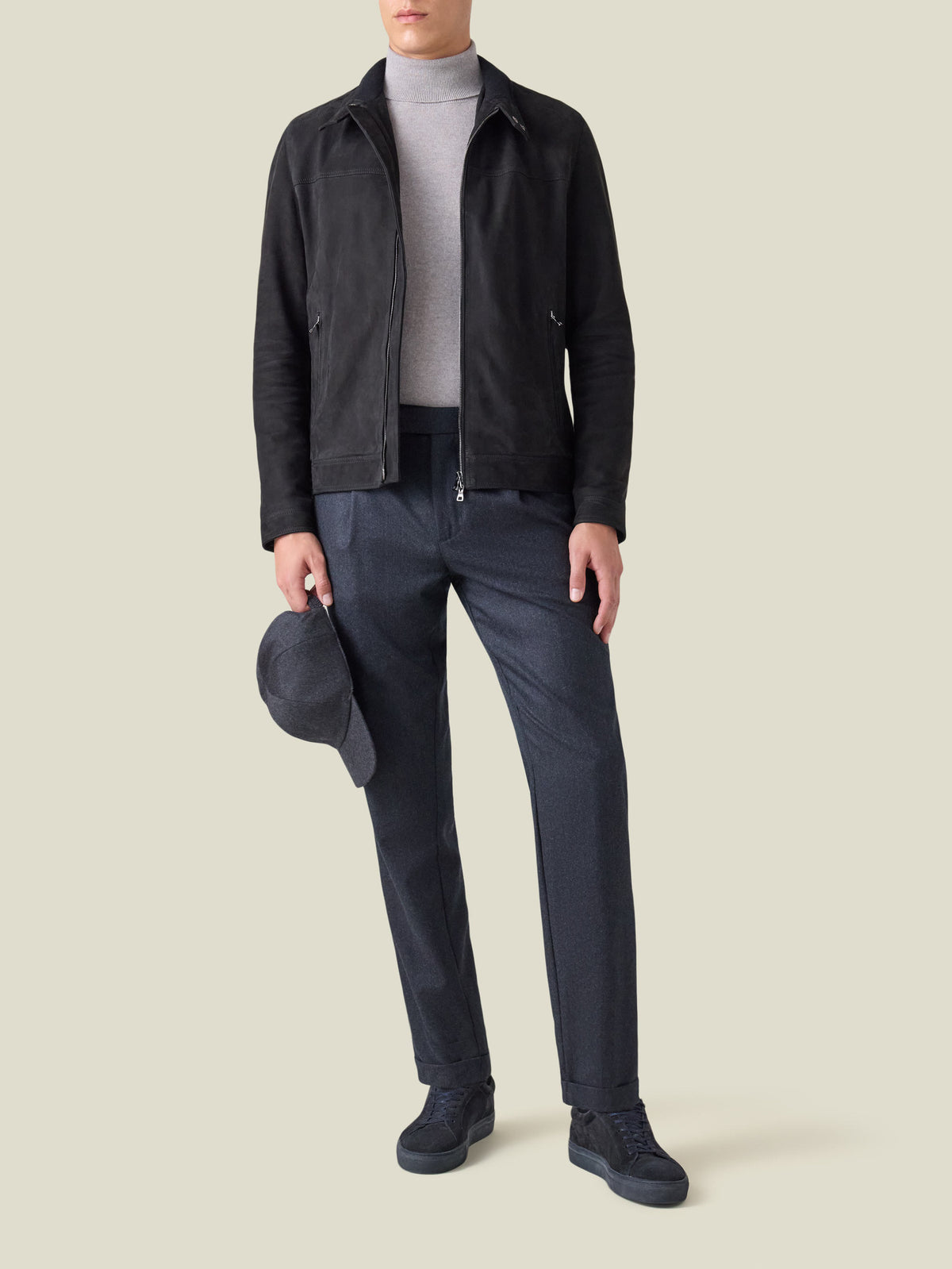 Model wears the Luca Faloni Classic Racer Jacket in black suede, with a grey turtleneck, navy trousers and matching sneakers.