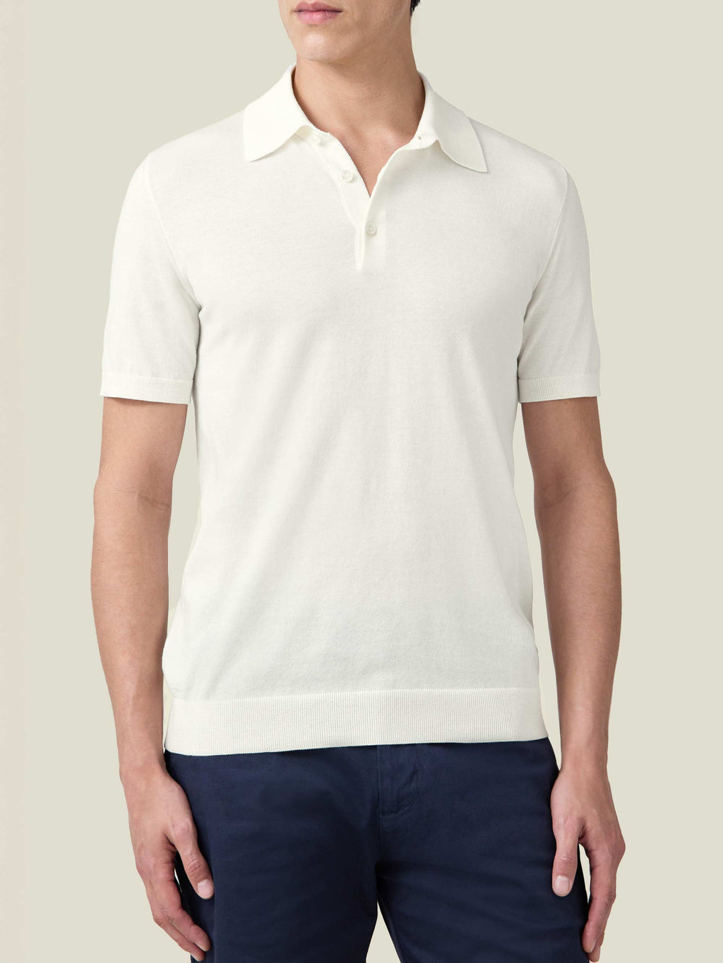 Front view of a man wearing the cream Knitted Cotton Polo with dark trousers.