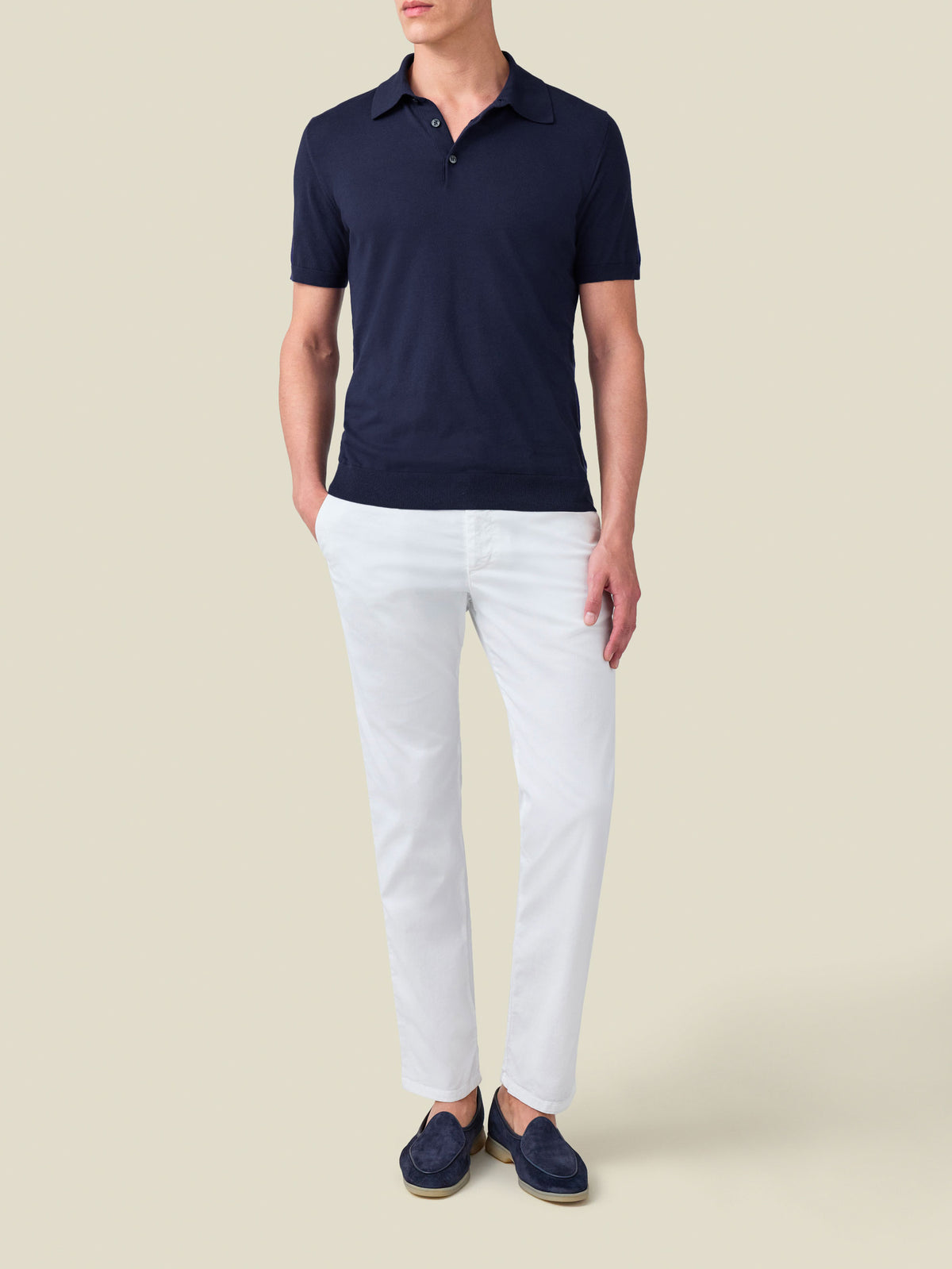 Full-length view of a model wearing the Knitted Cotton Polo in Midnight Blue with white trousers and navy loafers.