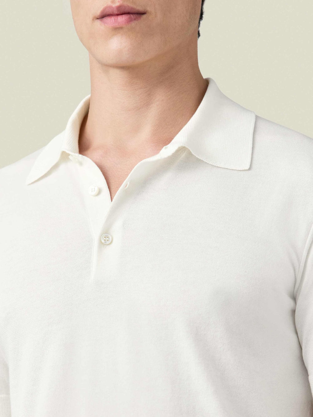 A close-up of a man modelling the cream Knitted Cotton Polo from Luca Faloni, showing the collar and fine knit detail.