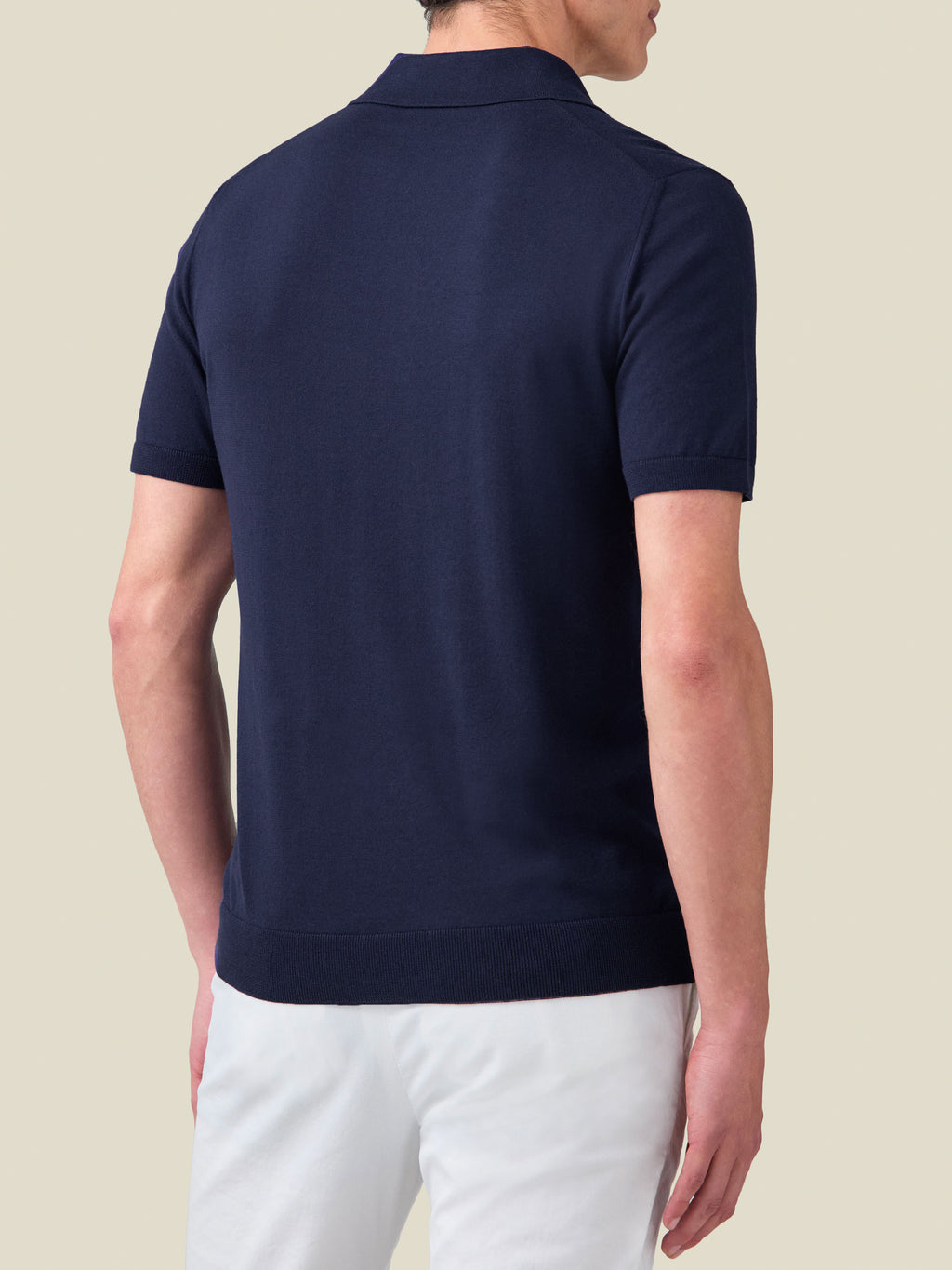 Back view of a man wearing the Luca Faloni Midnight Blue Knitted Cotton Polo with white trousers.