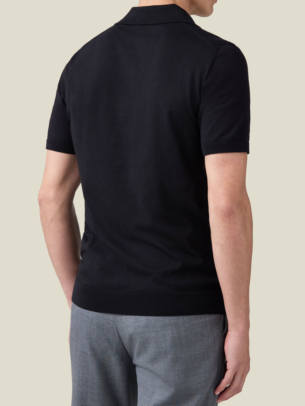 Back view of a model wearing the black Knitted Cotton Polo, highlighting its fitted silhouette and straight ribbed hem.
