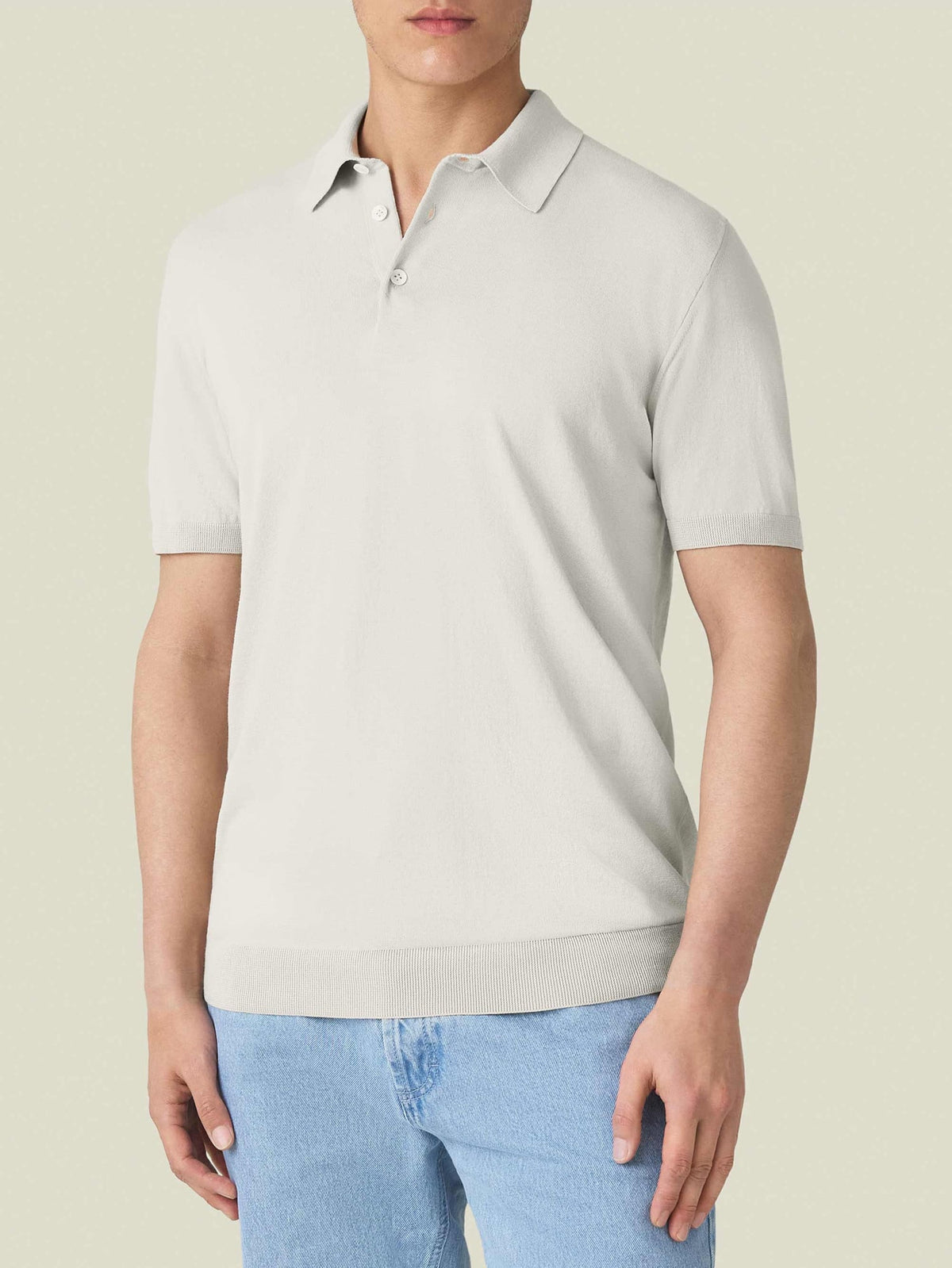 Front view of a model wearing the Knitted Cotton Polo in Sand, a short-sleeved top, paired with light blue jeans.