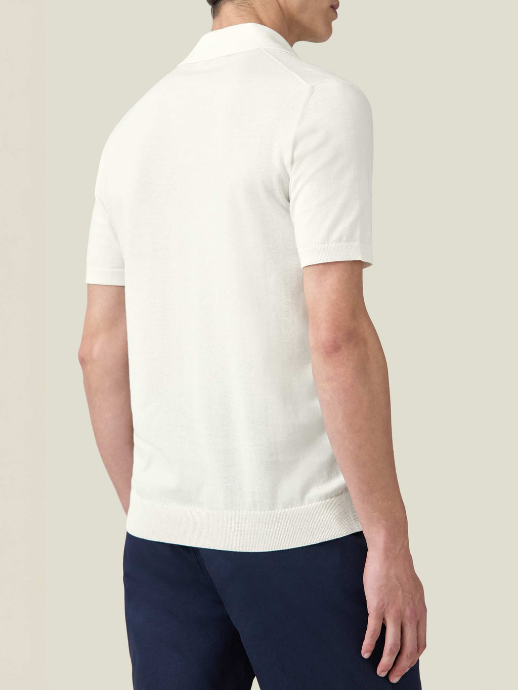 A rear three-quarter view of a model wearing the Luca Faloni cream Knitted Cotton Polo with navy trousers.