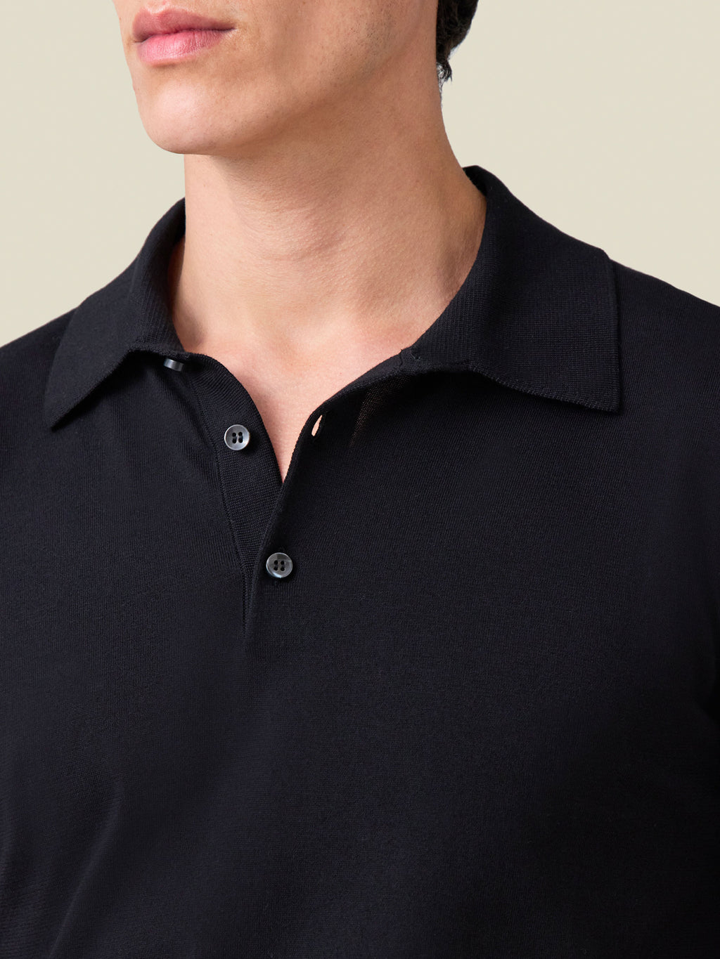 Close-up on the collar of the black Knitted Cotton Polo, showing the fine knit texture and mother-of-pearl buttons.