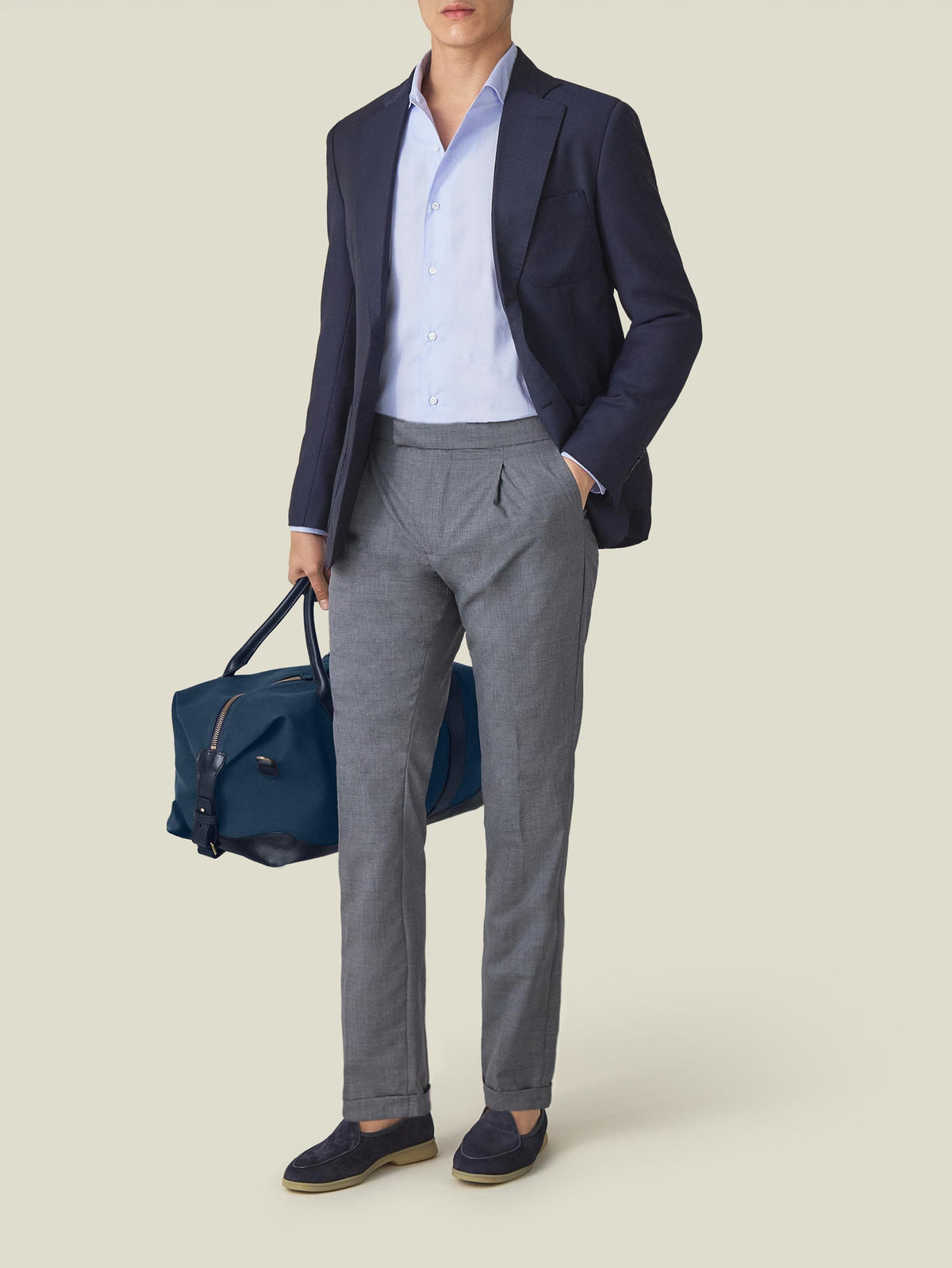 A model wears the Striped Light Blue Poplin Cotton Shirt styled with a navy blazer, grey trousers, and a navy travel bag.