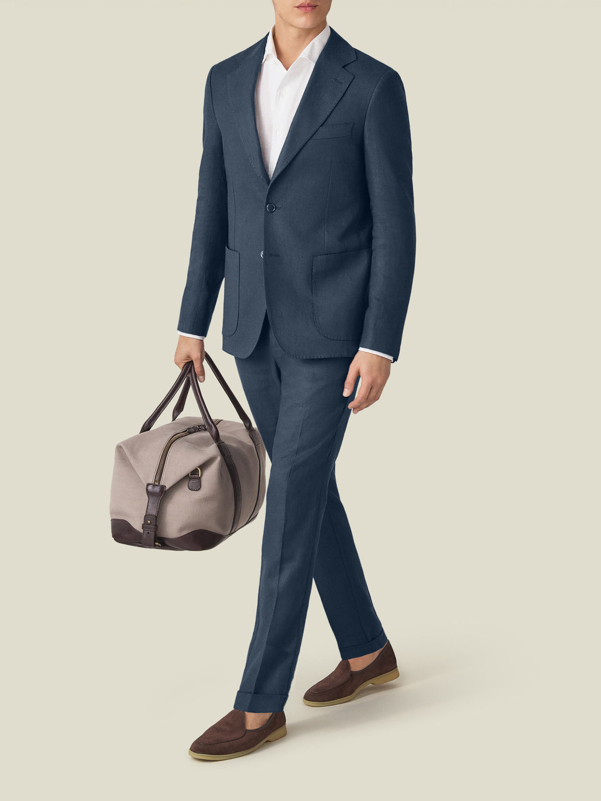 Model walks in the Luca Faloni Navy Blue Linen Suit with a white shirt, brown loafers, and a travel bag.