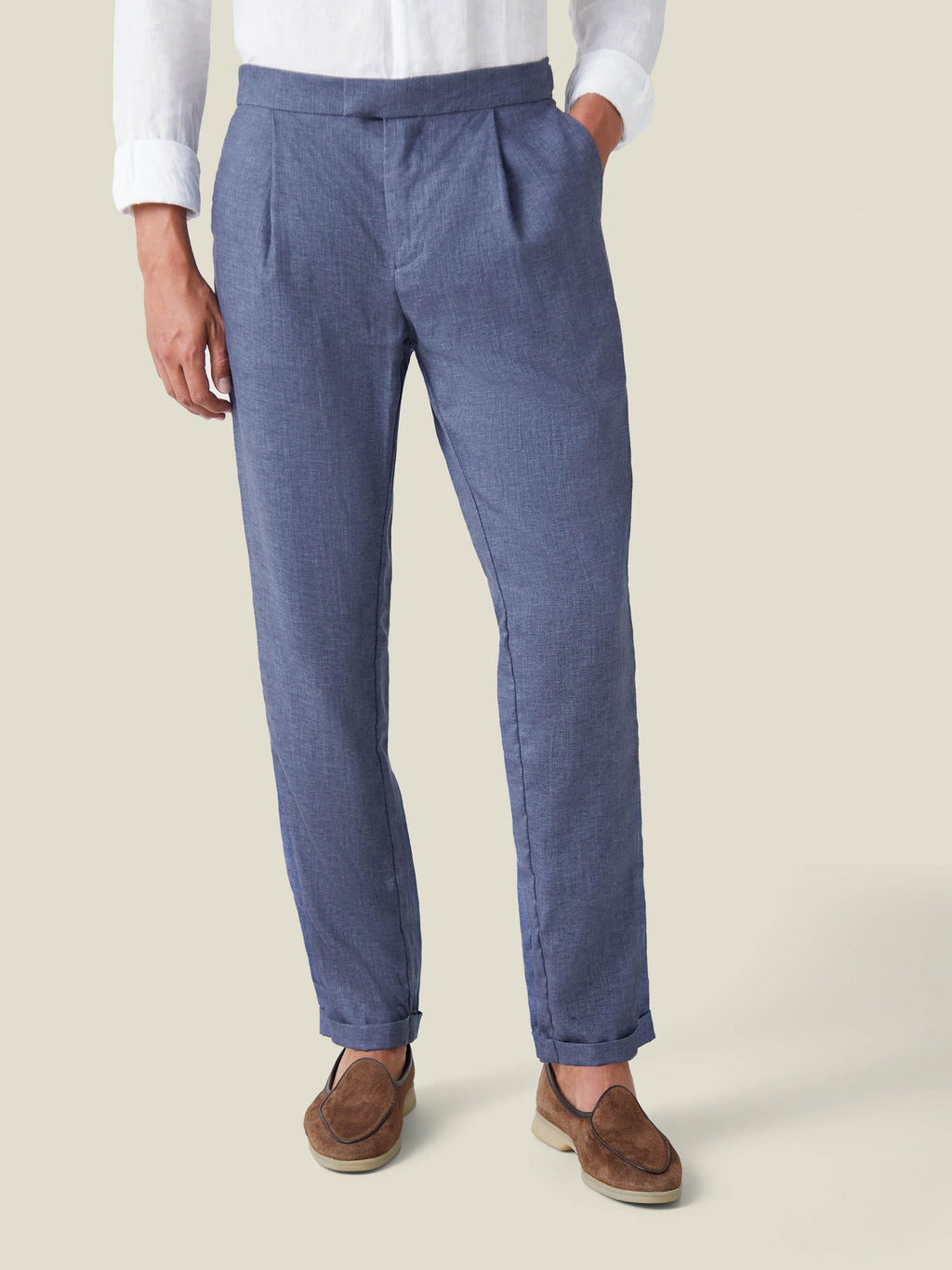 A man wears the melange blue linen trousers from the Azure Linen Suit, showing the pleated front and rolled cuffs.