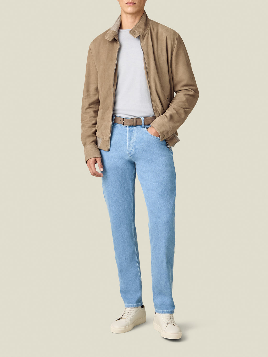 A model wears the Luca Faloni Cashmere Denim Jeans in light blue, styled with a beige suede jacket and white sneakers.