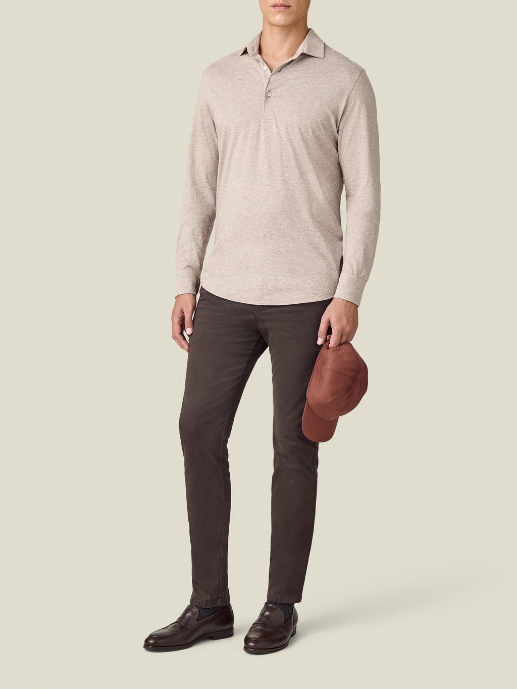 A model wears the Luca Faloni Cashmere-Cotton Long Sleeved Polo in Oatmeal, styled with dark brown trousers and loafers.