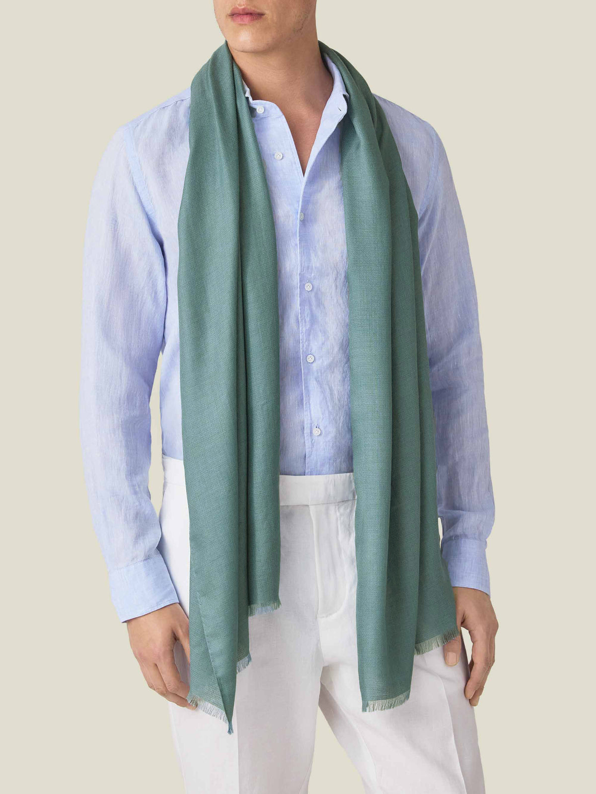 A front view of a model wearing the Luca Faloni Silk-Cashmere Scarf in Teal with a light blue shirt and white trousers.
