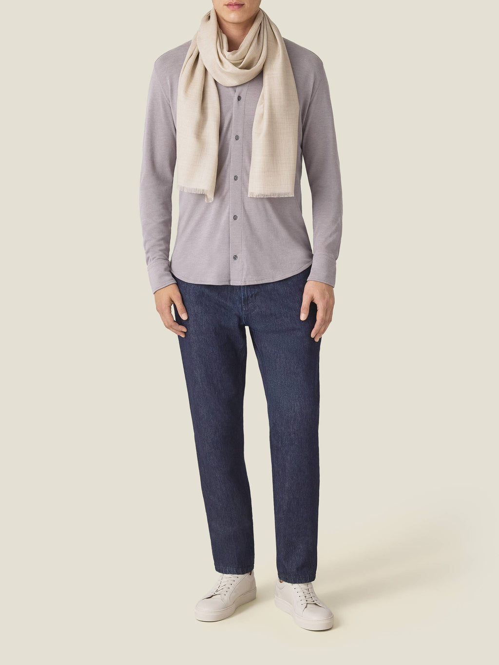 Man models the Luca Faloni sand silk-cashmere scarf, worn with a grey shirt, dark jeans, and white sneakers.