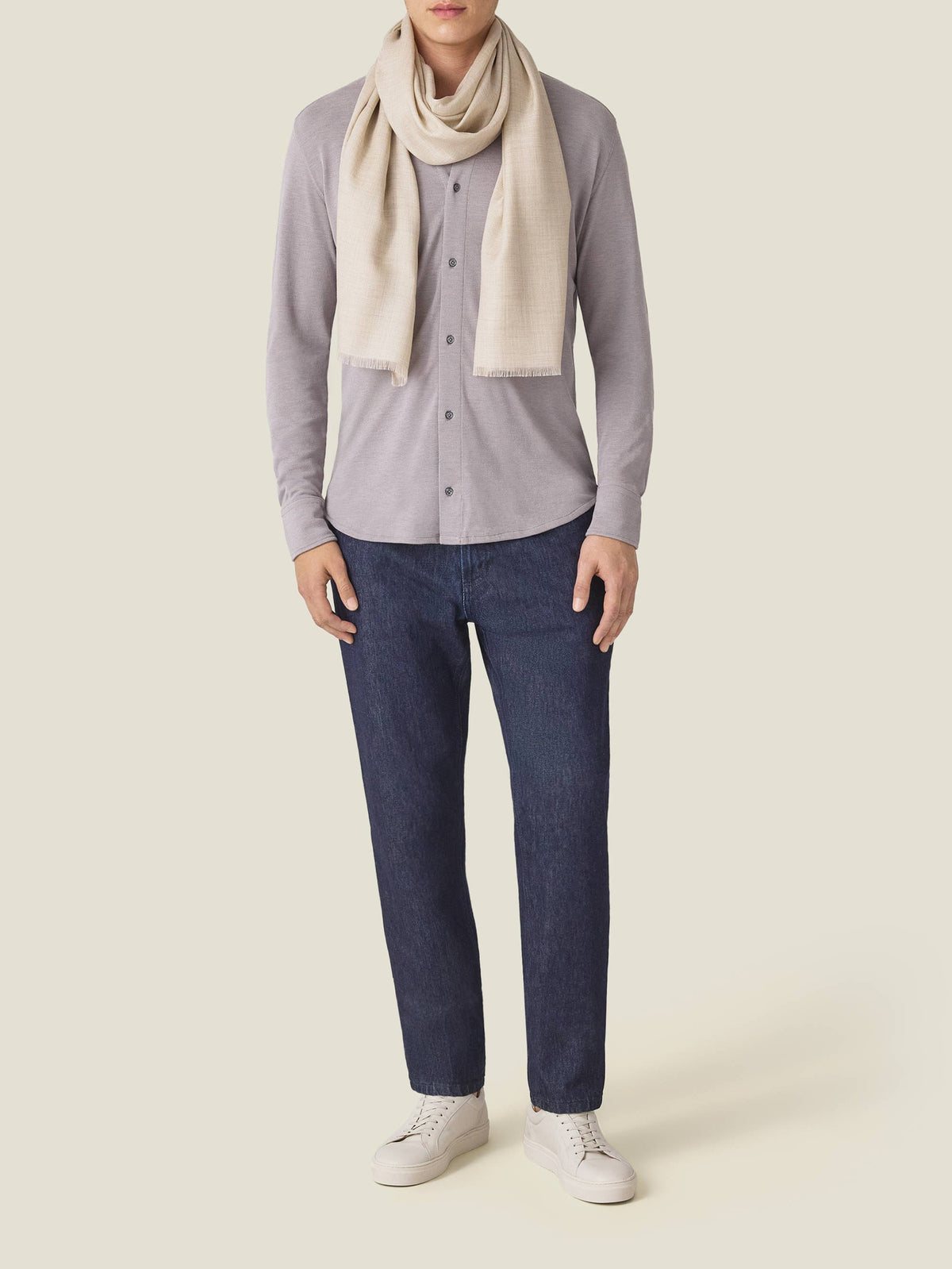 Man models the Luca Faloni sand silk-cashmere scarf, worn with a grey shirt, dark jeans, and white sneakers.