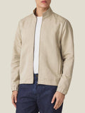 Front view of a model wearing the Luca Faloni Linen Bomber Jacket in Sand over a white t-shirt and dark blue jeans.