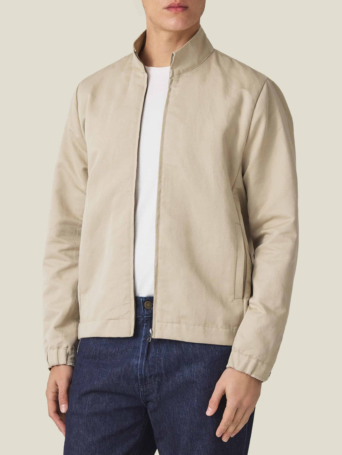 Front view of a model wearing the Luca Faloni Linen Bomber Jacket in Sand over a white t-shirt and dark blue jeans.