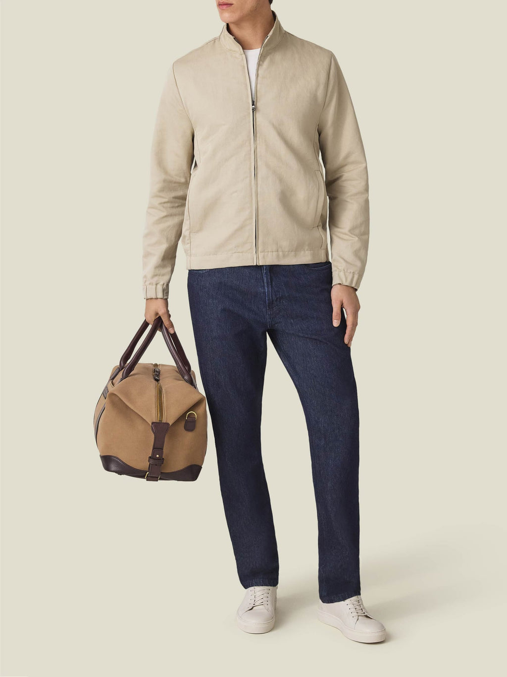 Full view of a model wearing the Luca Faloni Linen Bomber Jacket in sand, styled with dark jeans and a travel bag.